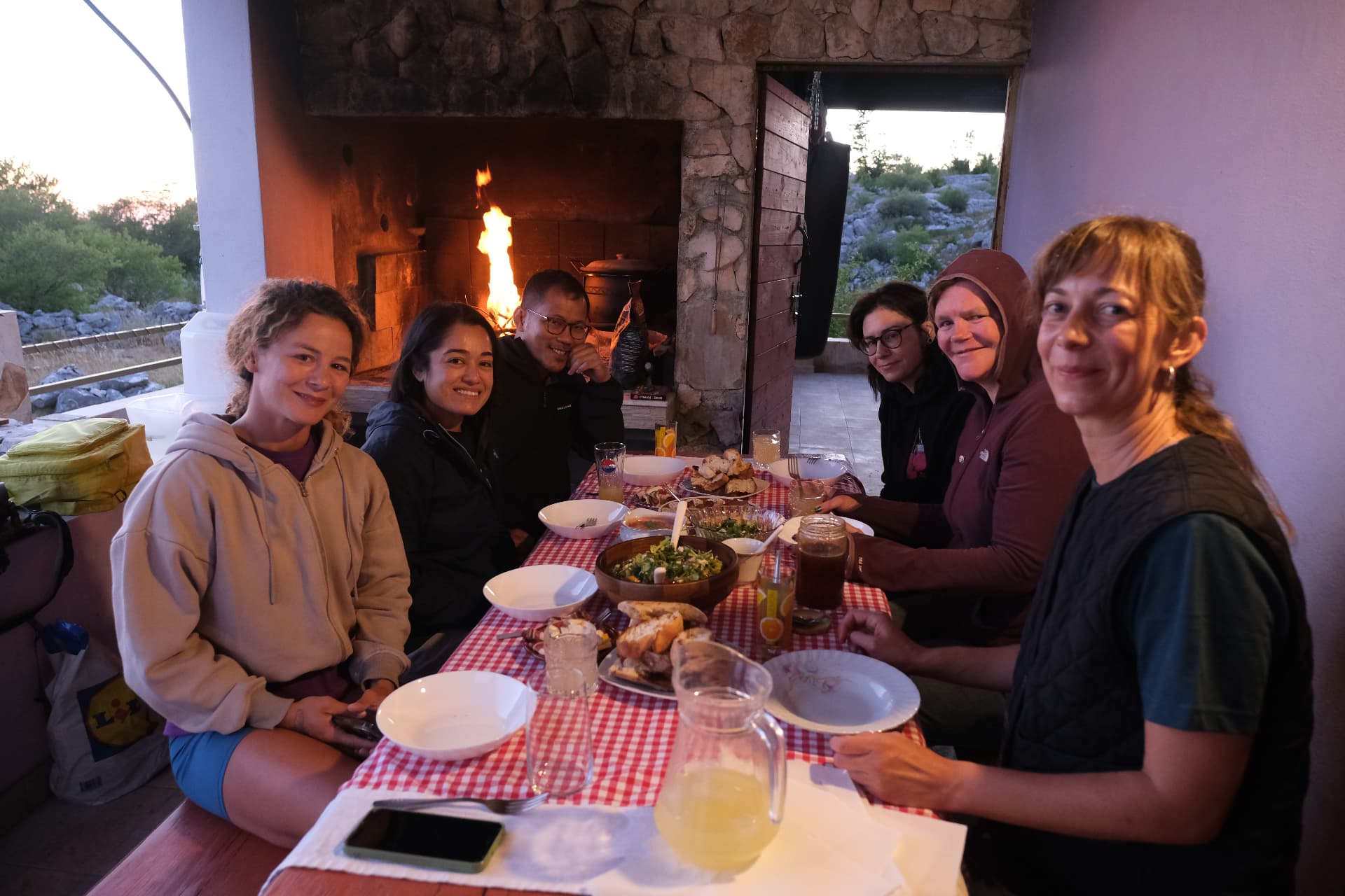 The group at the checkered table by the fire, plates of homemade food between them