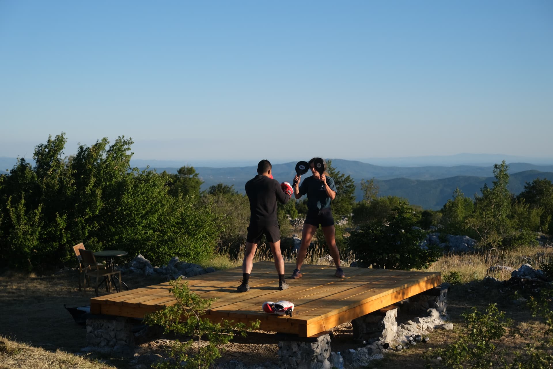 Coach holding target pads for a boxer on the raised platform, layered mountains behind
